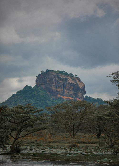 Scenic view of Sigiriya rock fortress amidst lush green nature under cloudy sky in Sri Lanka.