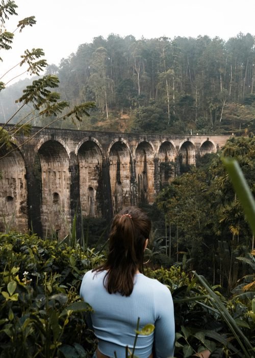 Explore the lush jungle surrounding the iconic Nine Arches Bridge in Ella, Sri Lanka, with a serene back view of a woman.