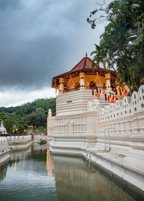 Beautiful view of a sacred temple reflecting in the river, surrounded by lush greenery, under a moody sky in Sri Lanka.