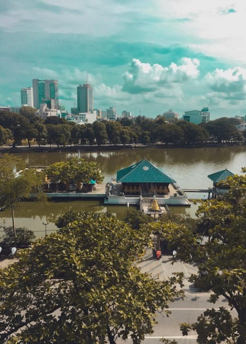 A stunning aerial cityscape featuring a peaceful lakeside temple with lush greenery and modern buildings.